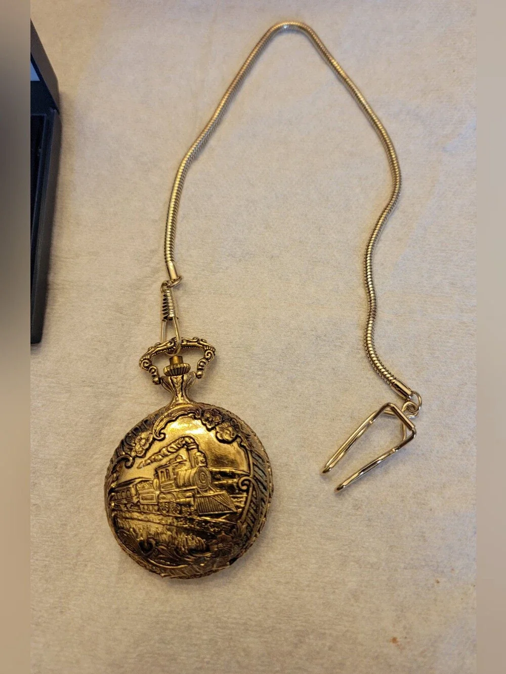 Vintage gold-tone pocket watch has a raised steam engine train motif.